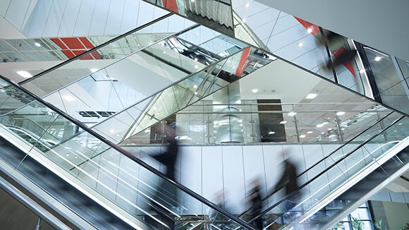 Four mirrored escalators crossing over in an office environment with business people