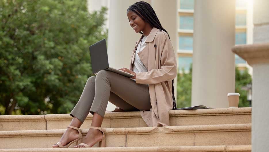 Steps, city and black woman typing on laptop in street, social media or internet browsing. Technology, computer or happy remote worker or business female working on research, email or project in town.