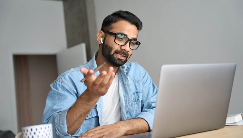 Young happy indian man in glasses having video call at home offi
